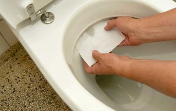 a person cleaning a toilet with a paper towel