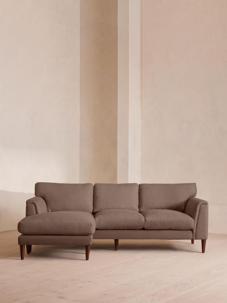 a large sectional couch sitting on top of a hard wood floor next to a white wall