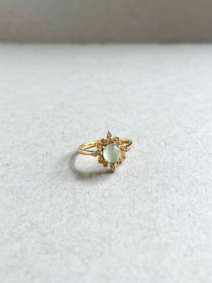 a gold ring with an opal stone in the center on a white surface,