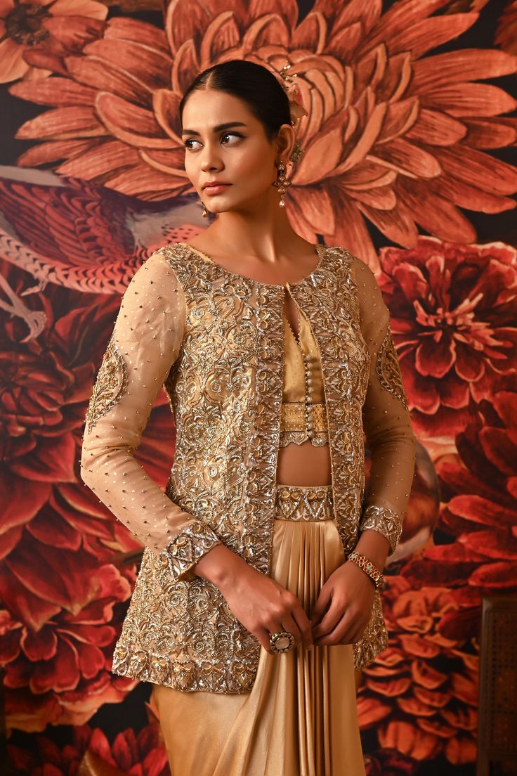 This Gold Co-ord set is the way to hop on the bold and versatile trend, that modern women prefer. Paired with a waistcoat style top along with a heavily embroidered jacket detailed with silver and golden hue and for the bottom a dhoti-style draped skirt giving you that chic regal look. Gold foil printed sleeveless blouse with embroidered border and handmade buttons on the centre front Front Open jacket with gold foil print heavily embellished with dabka & nakshi Waistcoat style bustier Dhoti-sty Reception Palazzo Set With Gold Embroidery, Designer Raw Silk Palazzo Set With Gold Embroidery, Traditional Designer Palazzo Set With Gold Embroidery, Designer Palazzo Set With Gold Embroidery For Eid, Reception Choli With Zari Work And Front Open, Front Open Choli With Zari Work For Reception, Festive Designer Palazzo Set With Gold Embroidery, Traditional Palazzo Set With Gold Embroidery For Designer Wear, Front Open Anarkali Set With Intricate Embroidery