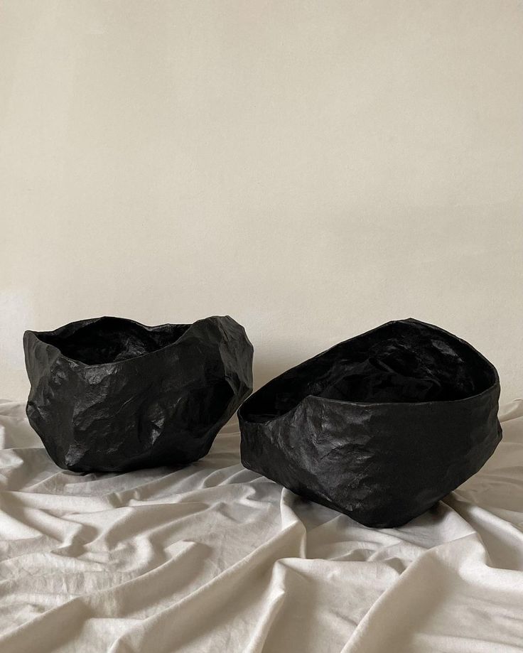 two black vases sitting on top of a white sheet