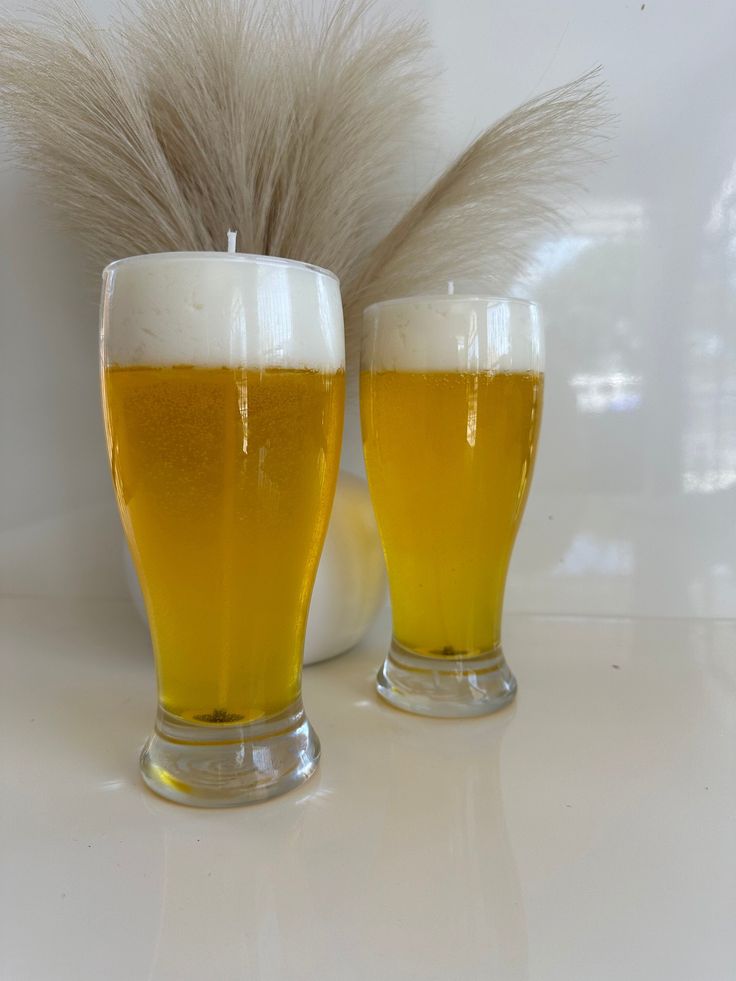 two glasses of beer sitting next to each other on a table with feathers in the background