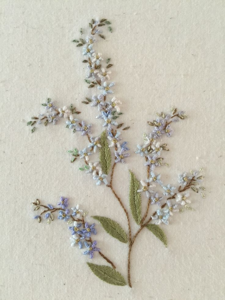 some blue and white flowers with green leaves on a beige surface, in the shape of a cross stitch pattern