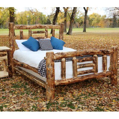 a bed made out of logs with blue pillows on it and two end tables next to it