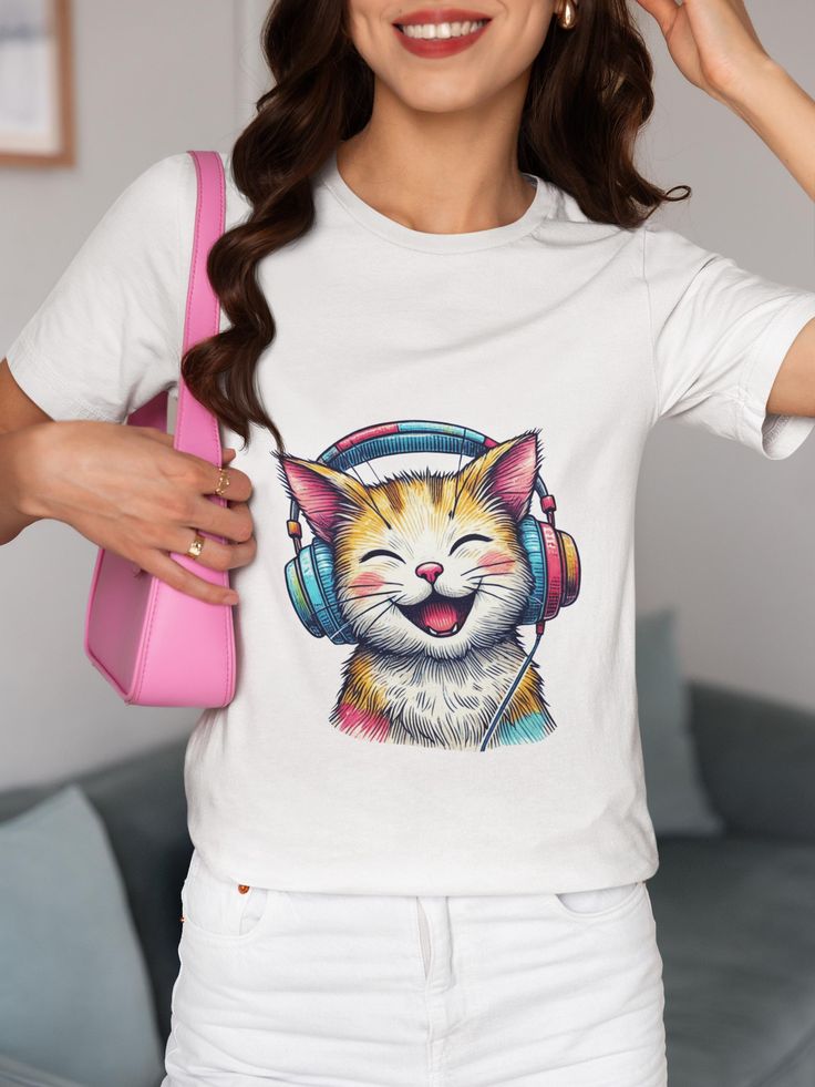 This unisex T-shirt features an adorable orange and white cat joyfully wearing oversized colorful headphones, perfect for both music enthusiasts and cat lovers. The vibrant, playful design makes this shirt a great addition to your casual wardrobe or as a unique gift for friends and family. Made with high-quality materials, it provides both comfort and style for any occasion. Express your love for music and felines in one fun graphic tee! We utilize the authentic Bella Canvas 3001 brand, renowned for its UNISEX design, making it one of the most sought-after shirts in the market. Prior to placing an order, kindly refer to our size chart. It can be located in both the listing's images and description. This cozy T-shirt serves as an ideal present, suitable for occasions such as birthdays, Chri White Cat Design T-shirt For Summer, White Summer T-shirt With Cat Design, White Cat Design T-shirt For Streetwear, White T-shirt With Cat Design For Streetwear, Trendy White T-shirt With Cat Print, Cat With Headphones, Orange And White Cat, Smiling Cat, Cool Graphic Tees