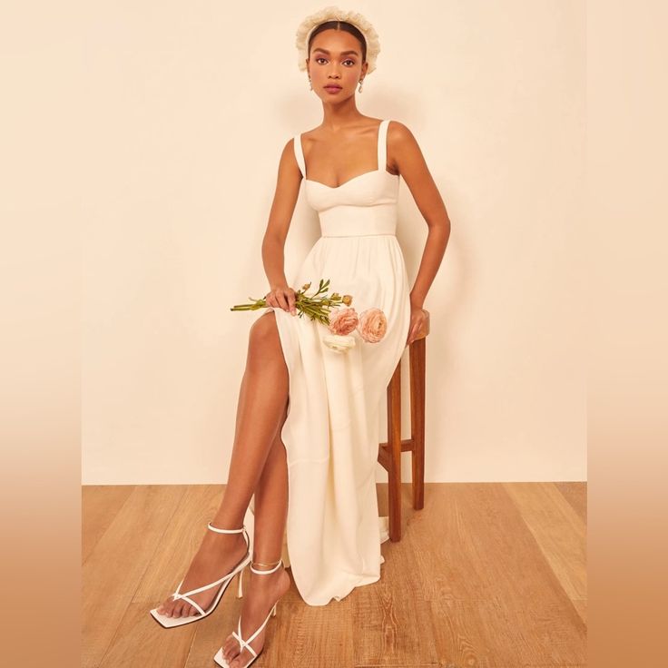 a woman is sitting on a chair wearing a white dress and holding a flower bouquet