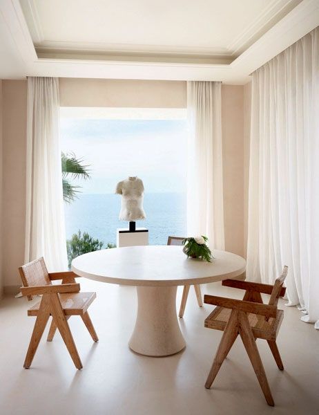 a white table and chairs in front of a large window with an ocean view behind it