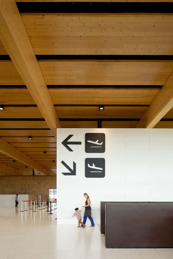 two people walking through an airport terminal with signs on the wall and ceiling above them