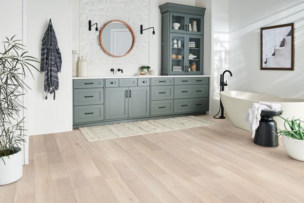 a bathroom with wood flooring and green cabinetry next to a bathtub in the corner