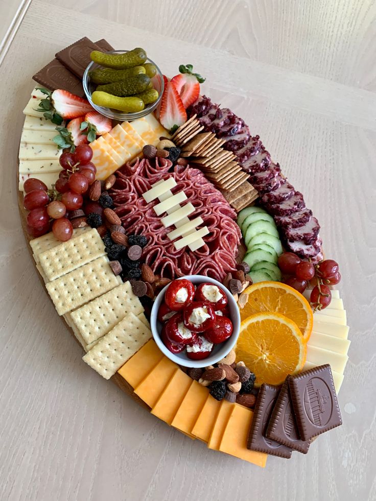 a platter filled with cheese, crackers, fruit and meats on a white table