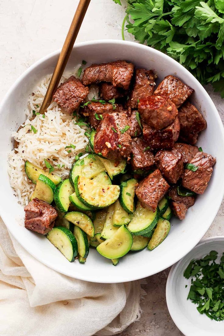 a bowl filled with meat and zucchini on top of rice next to chopsticks