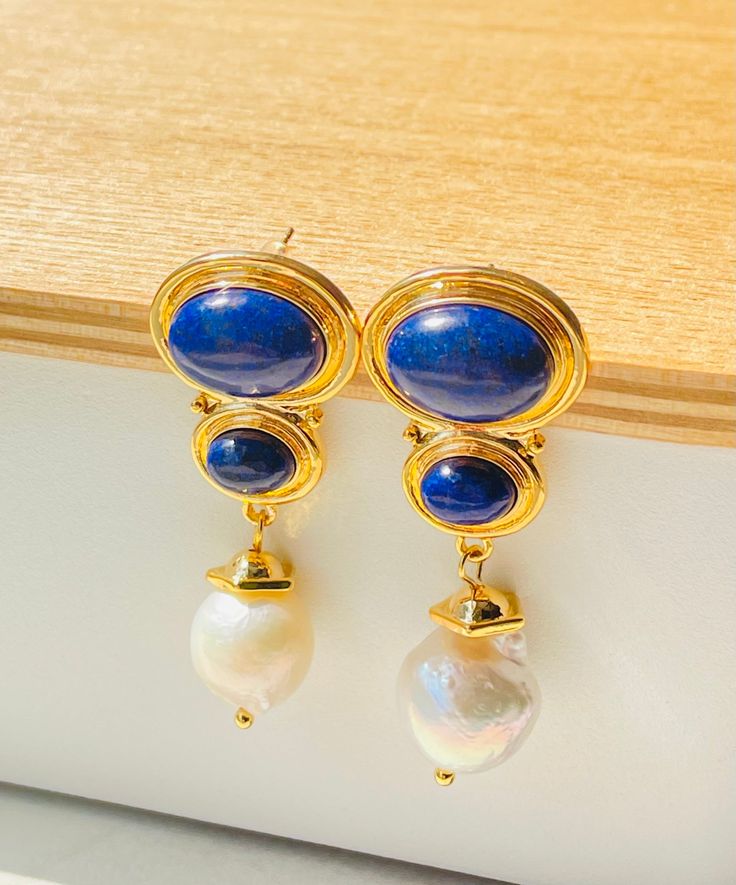 Lapis Lazuli Elegance Lustrous Gemstones: The Lapis Lazuli Elegance Earrings feature a design that embodies timeless beauty and contemporary grace. The deep blue Lapis Lazuli stones, known for their association with wisdom and truth, serve as the centerpiece, exuding an air of elegance and mystery. A delicate pearl drop enhances the design, adding a touch of luster and sophistication. Delicate Pearl Accent: Lapis Lazuli Elegance Earrings, a harmonious fusion of sophistication and the mesmerizing Blue Gemstone Luxury Pearl Earrings, Blue Luxury Pearl Earrings With Gemstone, Luxury Blue Gemstone Pearl Earrings, Luxury Blue Pearl Drop Earrings, Classic Blue Pearl Drop Earrings, Blue Lapis Lazuli Earrings For Formal Occasions, Formal Blue Lapis Lazuli Earrings, Elegant Gold Lapis Lazuli Earrings, Elegant Sapphire Earrings With Natural Stones