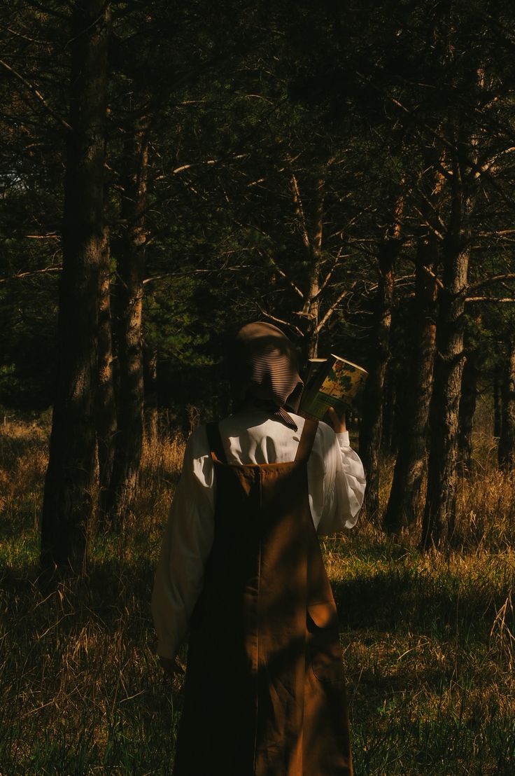 a person standing in the woods holding an object up to their face with both hands