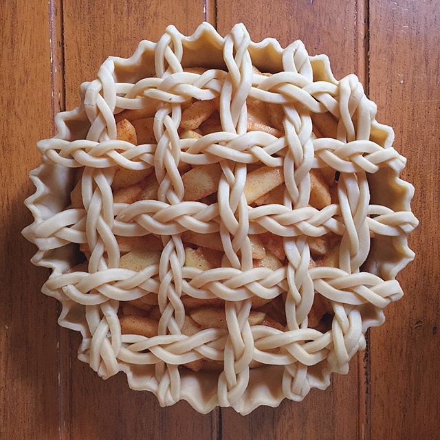 an apple pie with braided edges on a wooden surface