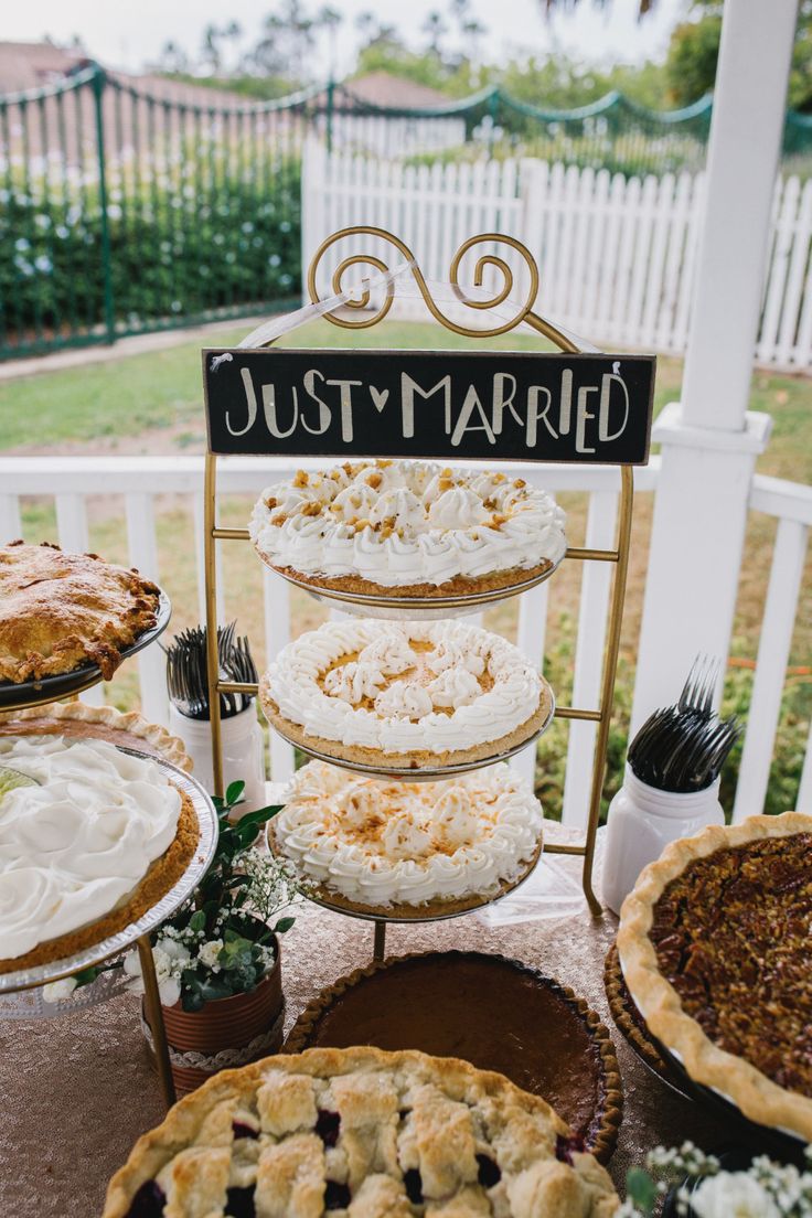 a table topped with pies covered in frosting next to a sign that says just married