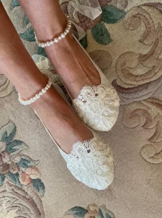 a woman's feet wearing white shoes and pearls