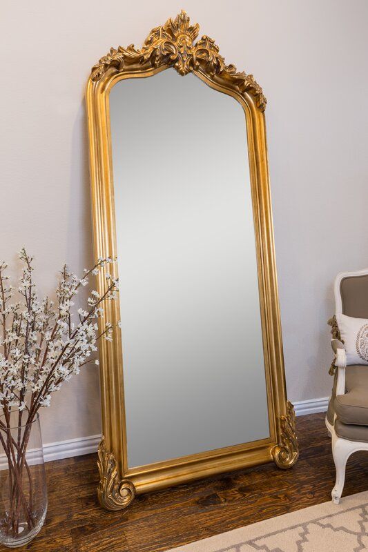 a large gold framed mirror sitting on top of a wooden floor next to a chair