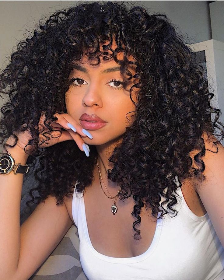 a close up of a person with curly hair wearing a white tank top and bracelets