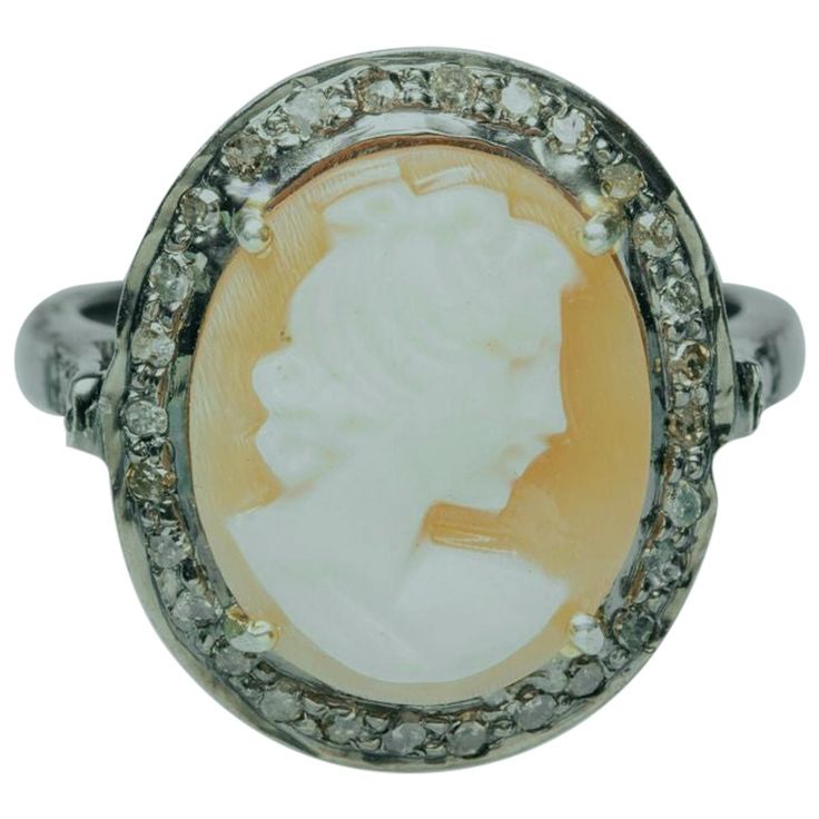 A lovely modern cameo ring set in sterling silver. The hand-carved shell depicts the profile of a woman with intricate detail facing to the right with a nice translucence when held up to the light. It is bordered with round, brilliant cut diamonds in a pave' setting and similar diamonds along the cathedral side portion of the ring. Diamond weight is .39 carats. Ring size is 7.25. The truest depiction in the photographs is the one on the human hand as the others are slightly overexposed. Amethyst Set, Cameo Ring, Carved Shell, February Birthstone, Pave Setting, February Birth Stone, Brilliant Cut Diamond, Cocktail Rings, Sterling Silver Ring