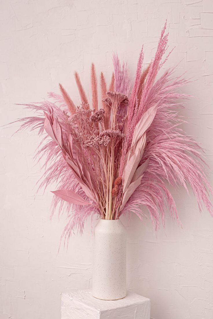 a white vase filled with pink feathers on top of a table