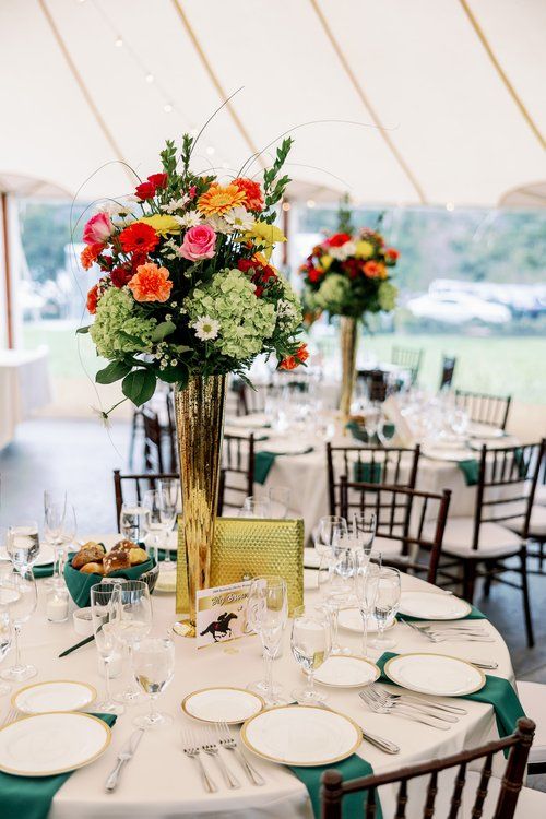 a table set up with plates, silverware and flowers in a tall gold vase