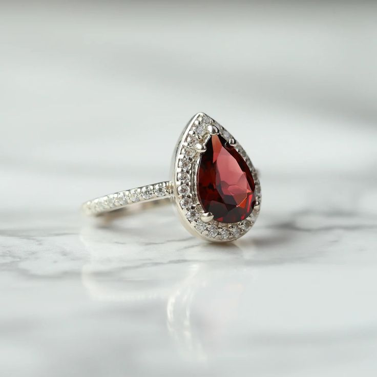 Looking for a ring that just demands attention? The Britney ring will definitely draw eyes, with a spectacular design and colorful Garnet as the main stone, bedazzled with moissanite. A truly unique ring to treat yourself to. Details: Center stone Gemstone: Garnet Stone Shape: Pear Measurements: approx. 10x7mm Side stones Gemstone: Moissanite Shape: Round Measurements: 1.3mm (37) Band measurements: approx. 1.8mm wide, approx. 1.5mm thick Pictured in vermeil, available also in sterling silver or Planet Ring, Draw Eyes, Moss Agate Ring, Rose Quartz Ring, Garnet Ring, Garnet Stone, Swiss Blue Topaz, Agate Ring, Unique Ring