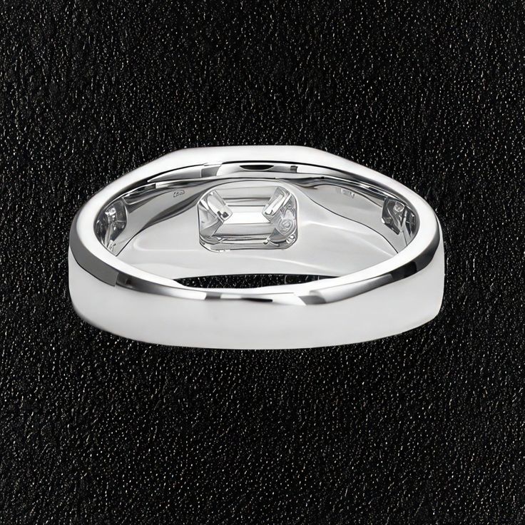 a white gold ring with an emerald cut diamond in the center on black leather background