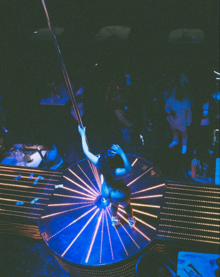 a woman holding an umbrella standing on top of a blue light filled table in the dark