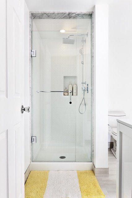 a white bathroom with yellow rugs on the floor and a shower stall in the corner