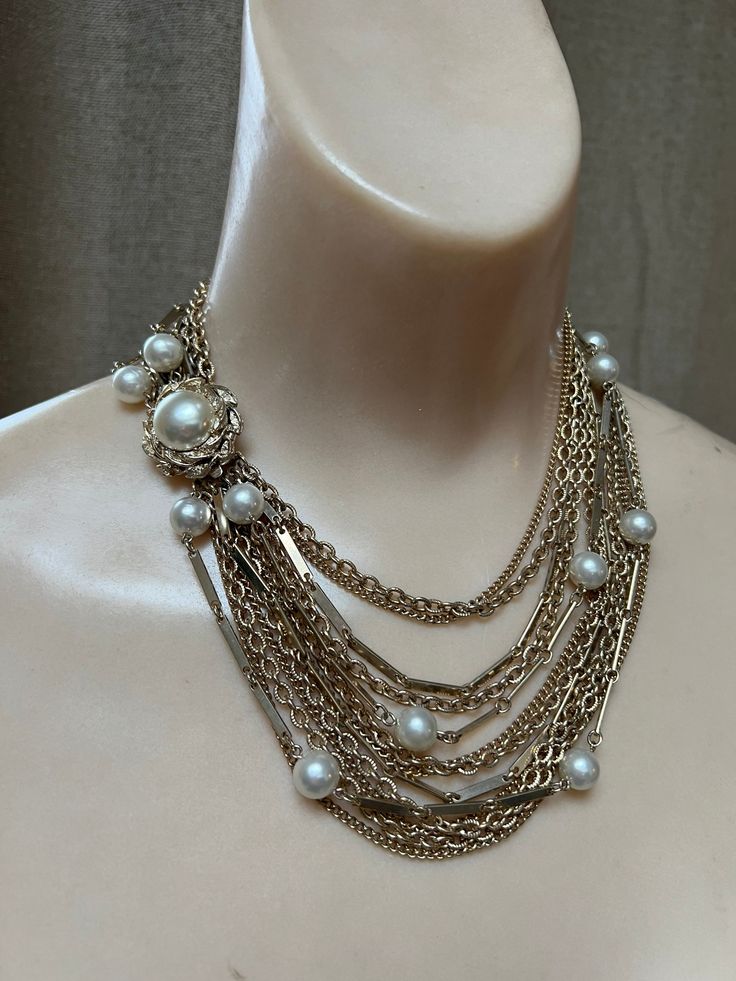 "Wonderful statement necklace for the woman who takes her necklaces seriously.   No name but truly, not needed. Total 12 chains with 2 strands featuring creamy ivory faux pearls about 8mm each. Variety of delicate goldtone chains in different sizes.  Most are a variation of curb links, some textured. Lovely large slide insert clasp to position as you like, perhaps on the side/front of the body.  Clasp measures 1\" diameter. I usually offer coodinating earrings but the ones I have are very large Elegant Metal Layered Necklace With Chain, Elegant Metal Bib Necklace With Chain Detail, Elegant Metal Bib Necklace With Chain, Chic Multi-strand Chain Jewelry, Multi-strand Metal Pearl Chain Jewelry, Elegant Metal Layered Necklace With Beaded Chain, Elegant Beaded Chain Metal Necklace, Elegant Layered Metal Necklace With Beaded Chain, Elegant Double Chain Metal Necklace