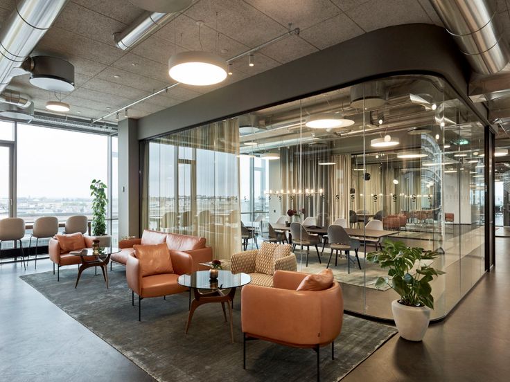 an office with glass walls and orange chairs in the center, looking out onto the city