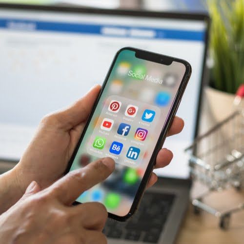 a person is holding an iphone in front of a laptop and computer screen with social media icons on it