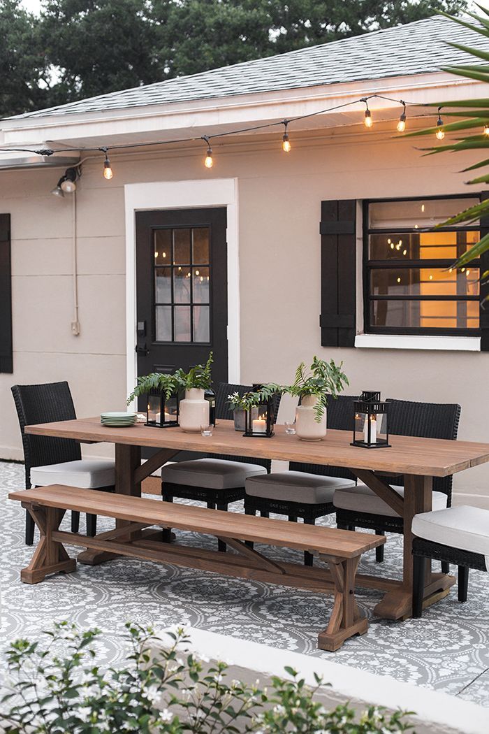 a wooden table sitting in front of a white house with black shutters on the windows