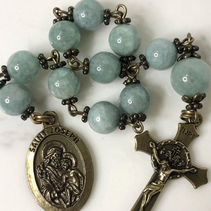 Handmade traditional Catholic single decade tenner rosary using green dyed jade smooth stone round beads. Antique bronze daisy bead caps on every bead with additional flower bead caps on Our Father bead. Antique bronze St. Joseph-Patron Saint of fathers, families and carpenters-Medal with Miraculous Medal Crucifix. Hail Mary beads are 8mm with the Our Father bead being 10mm. Designed to be used and/or displayed. Measures about 10" long. This rosary would make a beautiful gift for a baby shower, Baptism, First Communion, Confirmation, Father's Day, or any other special event or occasion. Comes in a beautiful black velvet pouch. I ship same or next business day. All of my rosaries are one of a kind and are my own personal creation. Photos are a part of the description-you will receive the ex Rosary With Natural Stones For Meditation, Natural Stone Rosary With Round Beads For Meditation, Spiritual Rosary Bracelet With Round Beads For Healing, Spiritual Healing Rosary Bracelet With Round Beads, 8mm Jade Beads For Spiritual Use, Round Beads Rosary With Natural Stones For Gift, Gift Rosary With Round Natural Stones, Spiritual Beaded Rosary For Jewelry Making, Green Beaded Spiritual Rosary