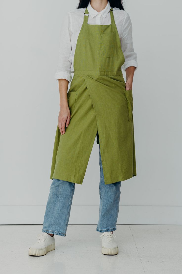 a woman standing in front of a white wall wearing green aprons and blue jeans