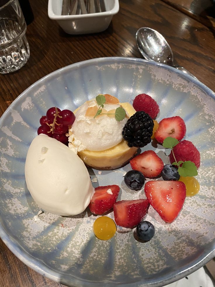 a plate topped with fruit and ice cream on top of a wooden table next to silverware