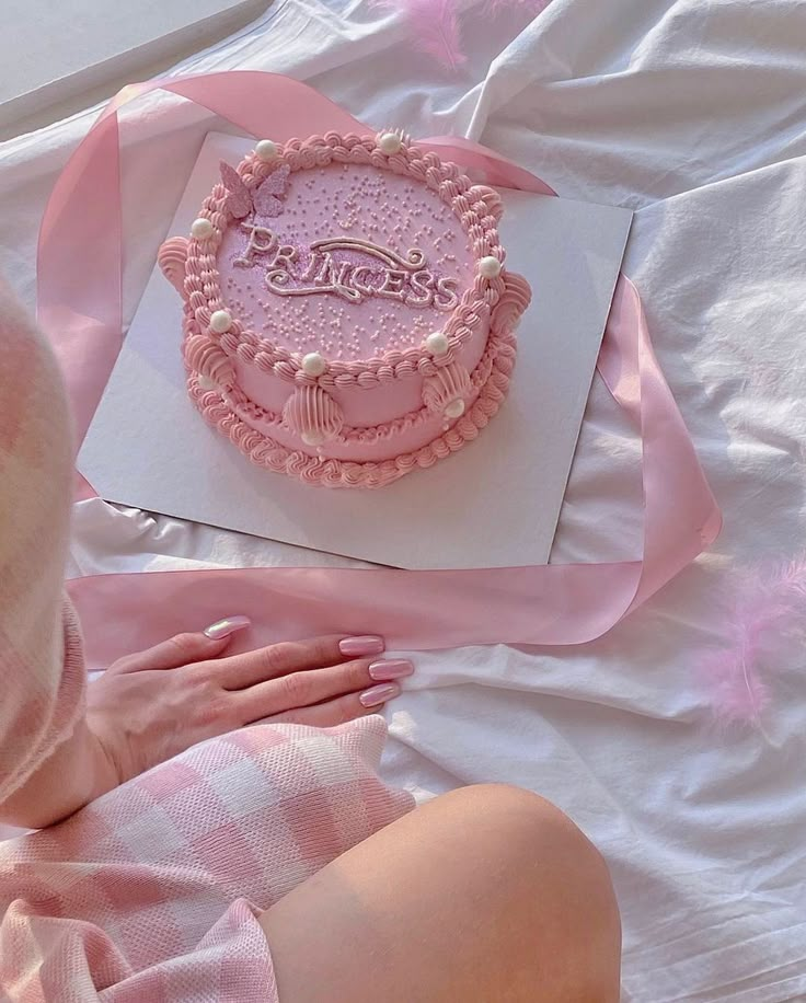 a pink cake sitting on top of a white sheet covered table next to a woman's hand