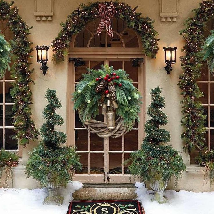 a christmas wreath on the front door of a house decorated with evergreens and bells