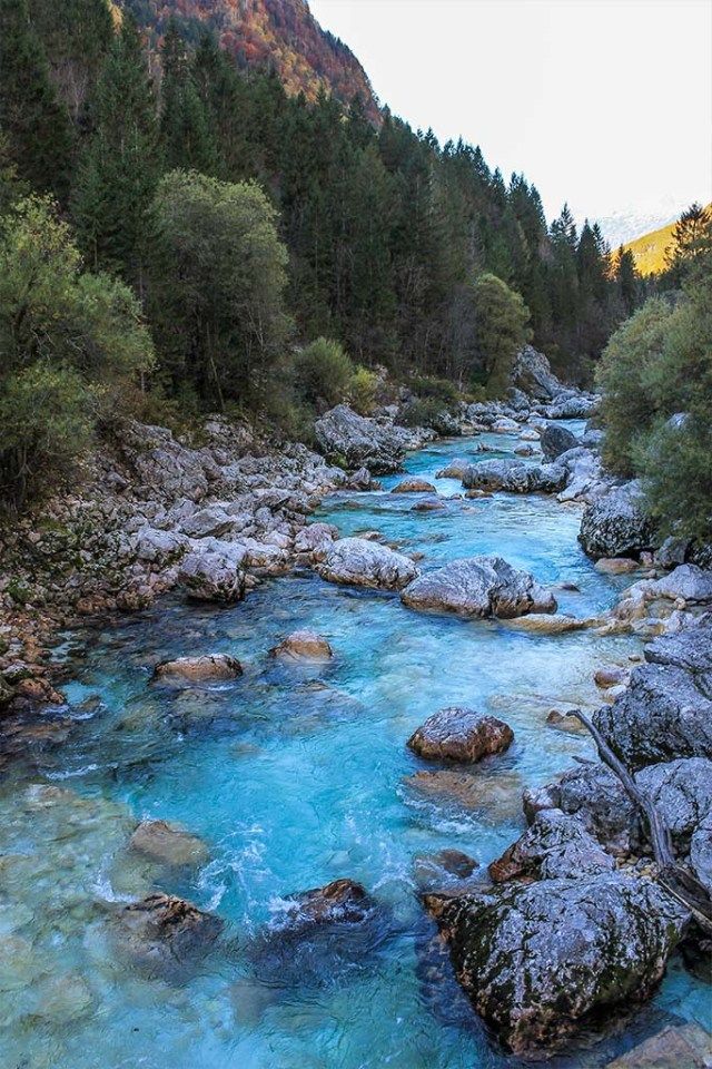 a river with blue water surrounded by trees and rocks in the middle of it's stream