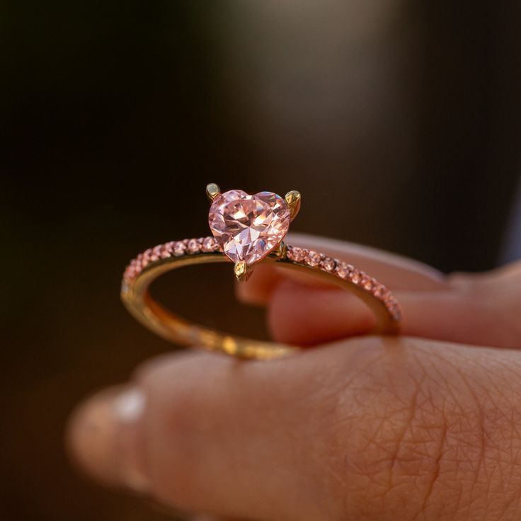 a close up of a person's hand holding a ring with a pink diamond