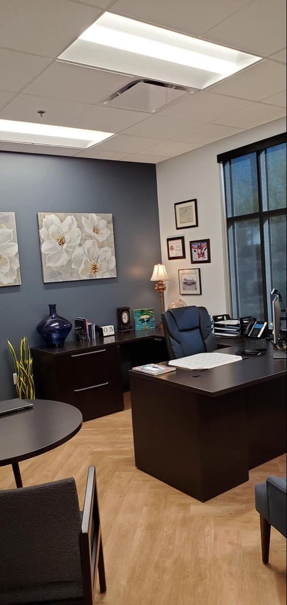 an empty office with chairs, desks and pictures on the wall above it's windows