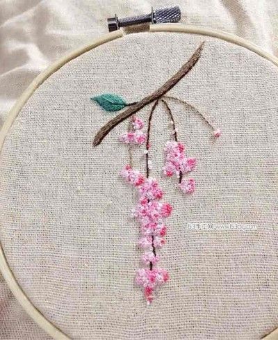 a close up of a embroidery on a piece of cloth with pink flowers and green leaves