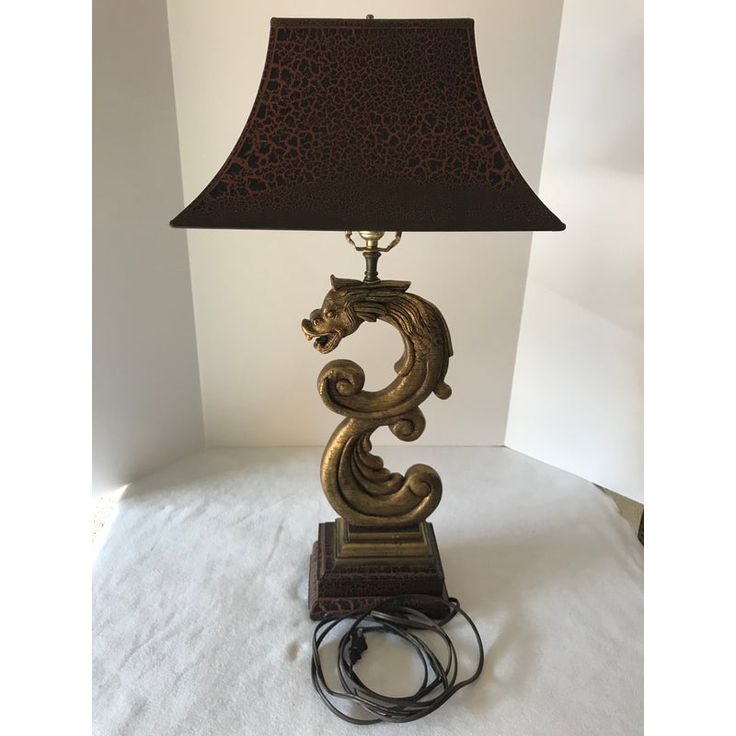 a lamp that is sitting on top of a white cloth covered tablecloth and has a brown shade over it