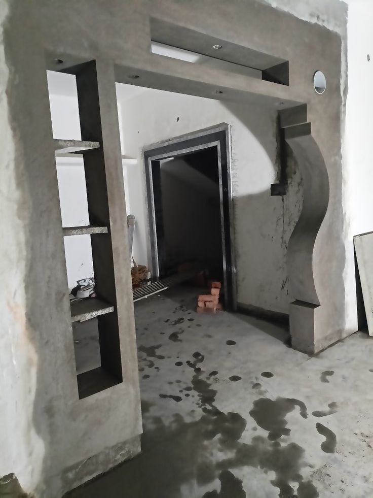 an unfinished room with concrete walls and shelves on the wall, in front of a doorway