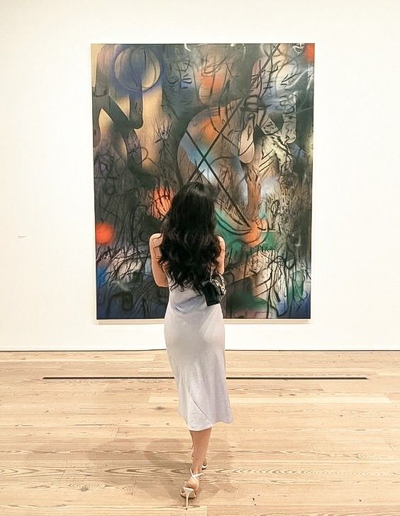 a woman standing in front of a painting on the wall with her back to the camera