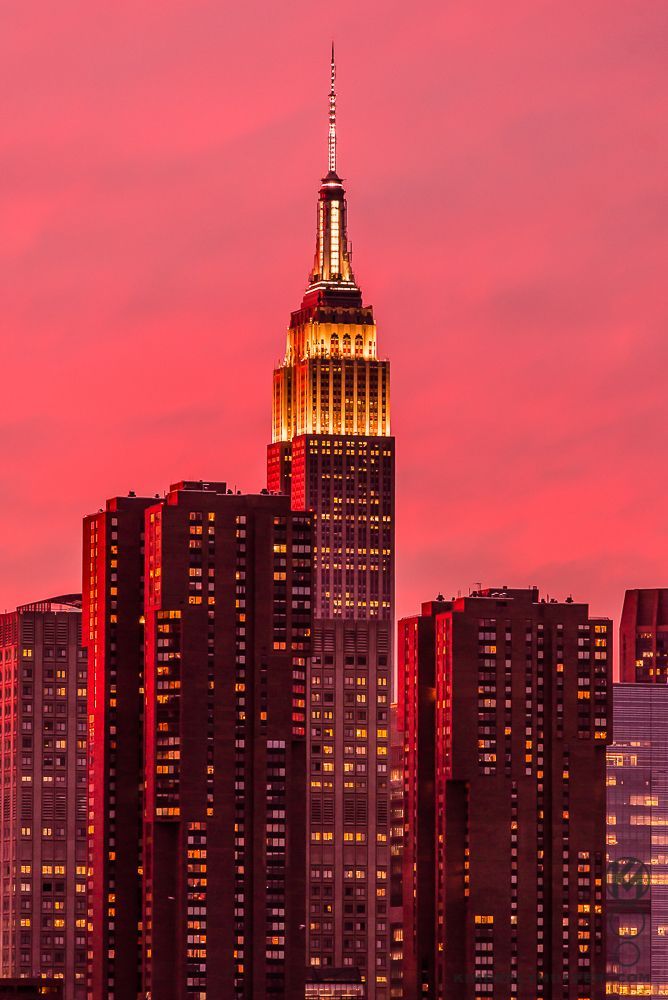 the empire building lit up at night in new york city, with other skyscrapers behind it