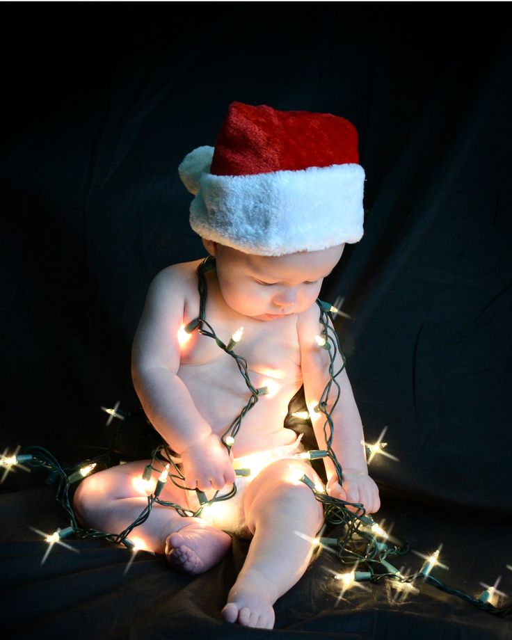 a baby wearing a santa hat sitting on top of a black blanket covered in christmas lights