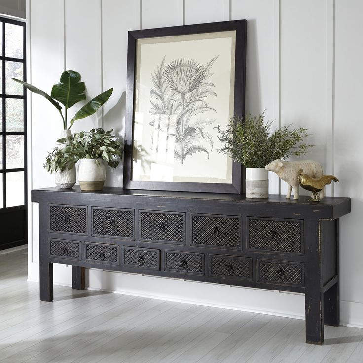 there is a black dresser with some plants on it and a framed picture above it