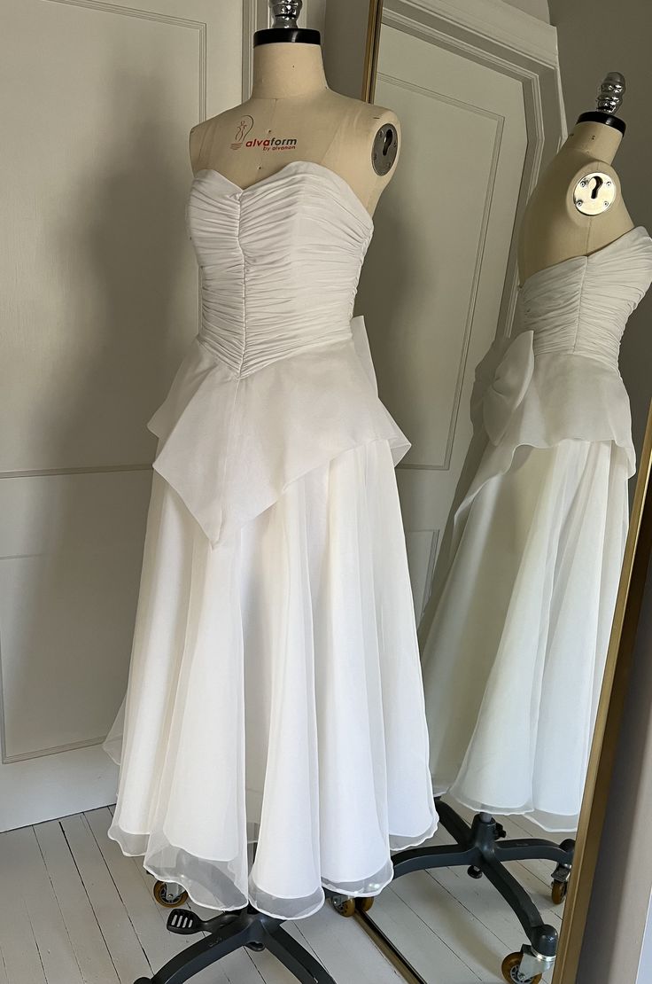 two white dresses are on display in front of a mirror, and one is wearing a dress with ruffles