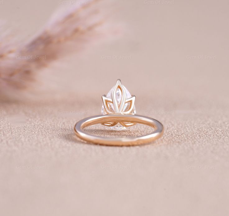 a gold ring with a leaf design on the front and side, sitting next to a feather